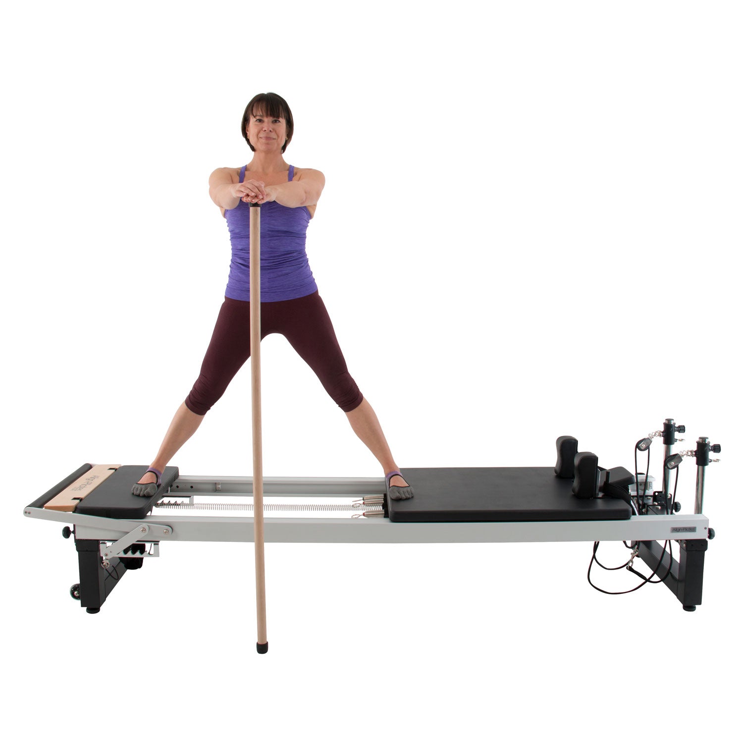 Frau nutzt die lange Align Pilates Pole aus Ahornholz zur Gleichgewichtshilfe auf dem Reformer