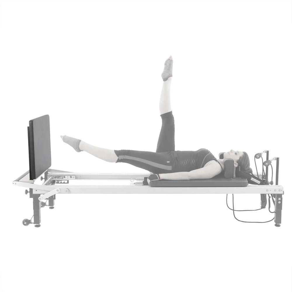 Frau bei einer Beinübung am Align-Pilates Jump Board – auf dem Reformer liegend mit Beinen in Scherenstellung an der Sprungplattform, Seitenansicht