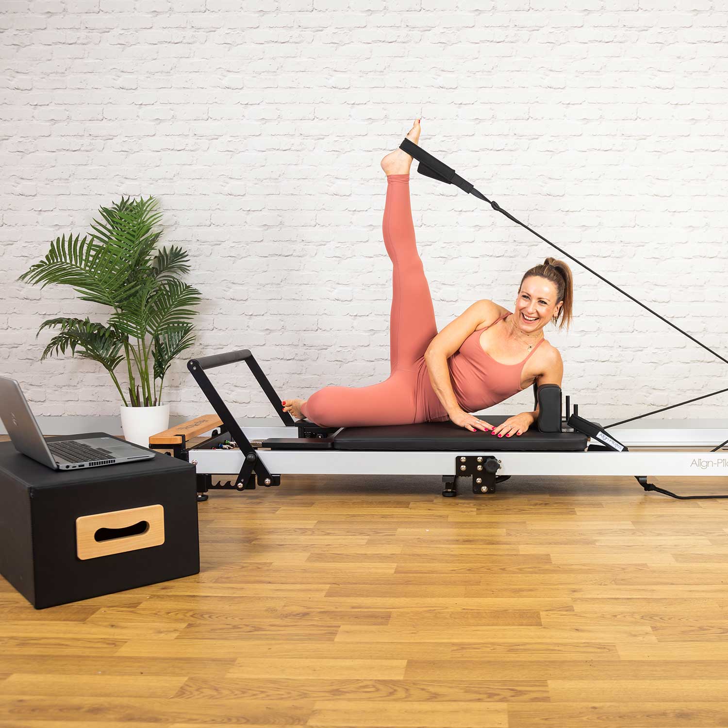 Frau bei einer seitlichen Beinübung auf dem aufgeklappten Align-Pilates F3 Folding Reformer – Heimtraining mit Fußschlaufe, Seitenansicht