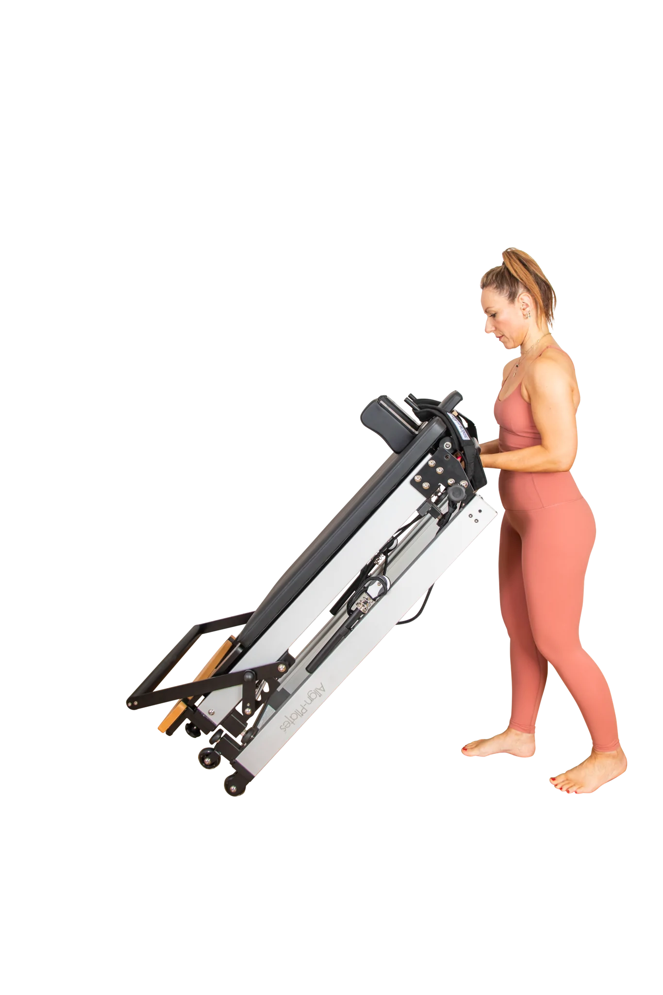Frau bewegt den zusammengeklappten Align-Pilates F3 Folding Reformer auf seinen Rollen – Demonstration der einfachen Mobilität im gefalteten Zustand