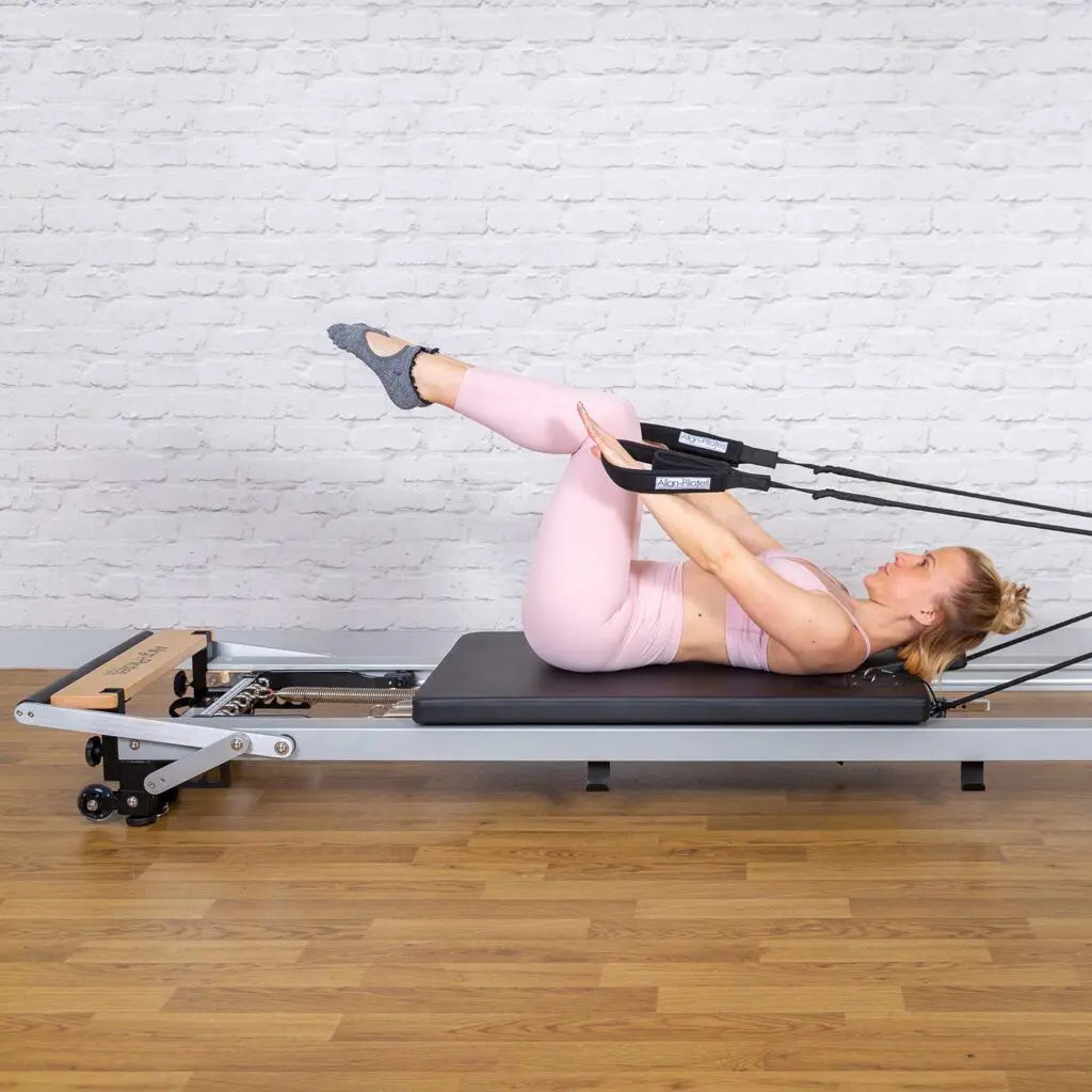 Frau bei einer Bauchübung auf dem tiefergelegten Align-Pilates A-Serie Reformer mit Low Legs – liegend mit Handschlaufen, Reformer nah am Boden, Seitenansicht