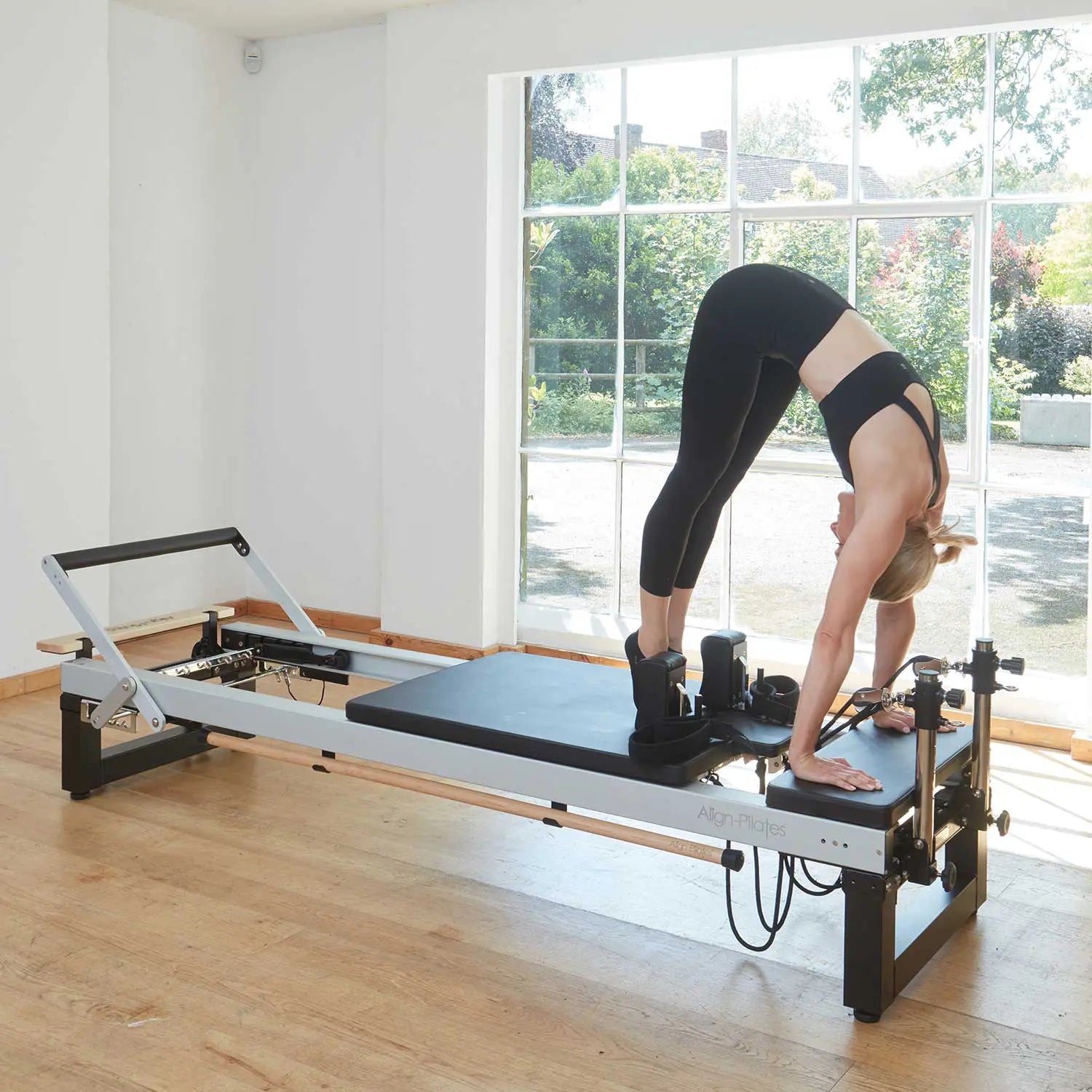 Frau bei einer stehenden Übung auf dem Align-Pilates A-Serie Reformer mit Standard Legs – Reformer auf 42 cm Arbeitshöhe, Seitenansicht