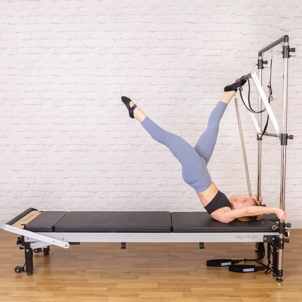 Frau bei einer Beinübung auf dem Align-Pilates Matratzen-Konverter am Reformer mit Tower – liegend auf der flachen Trainingsfläche, Seitenansicht