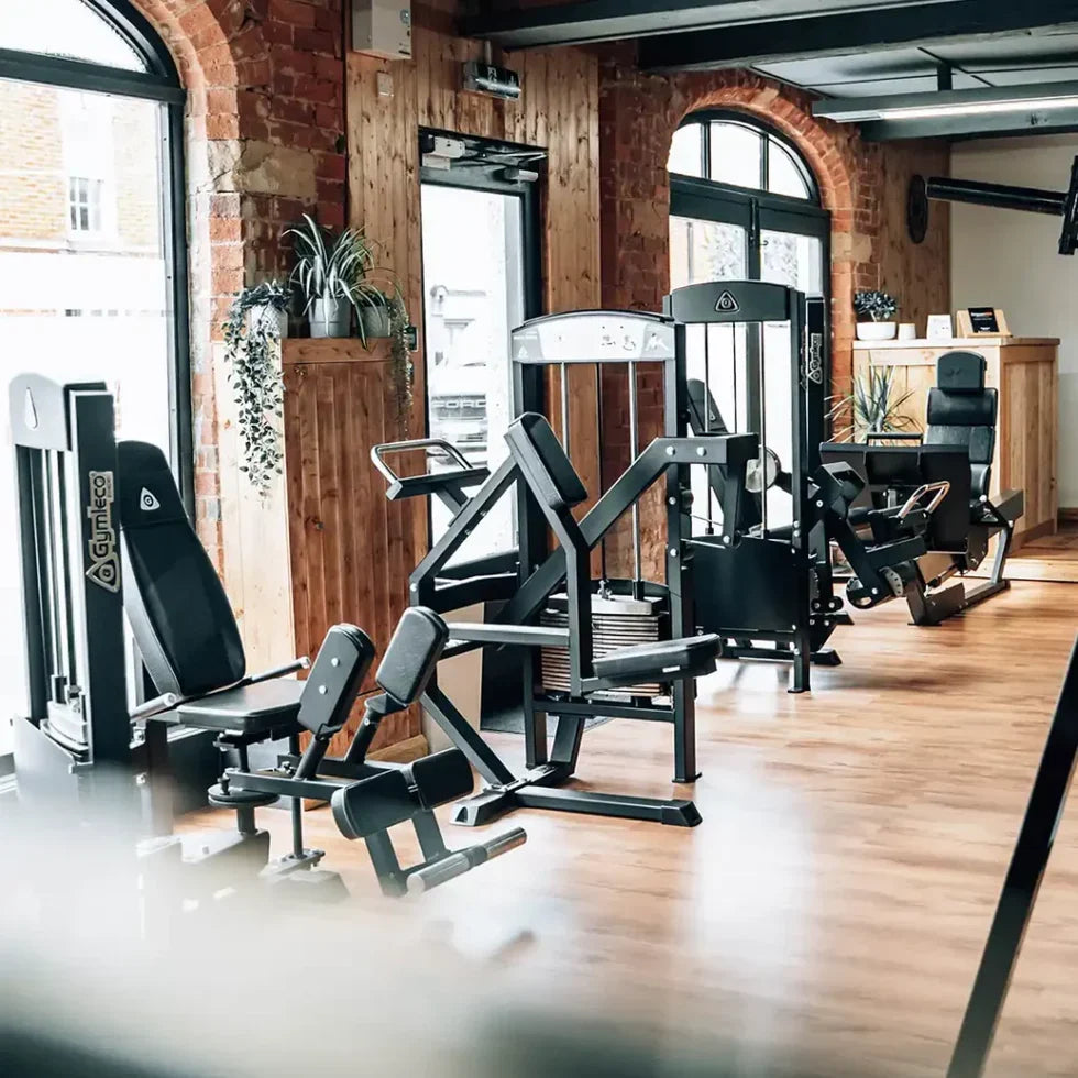 Gymleco-Kraftgeräte mit Steckgewichten in einem Studio mit Holzboden und Rundbogenfenstern