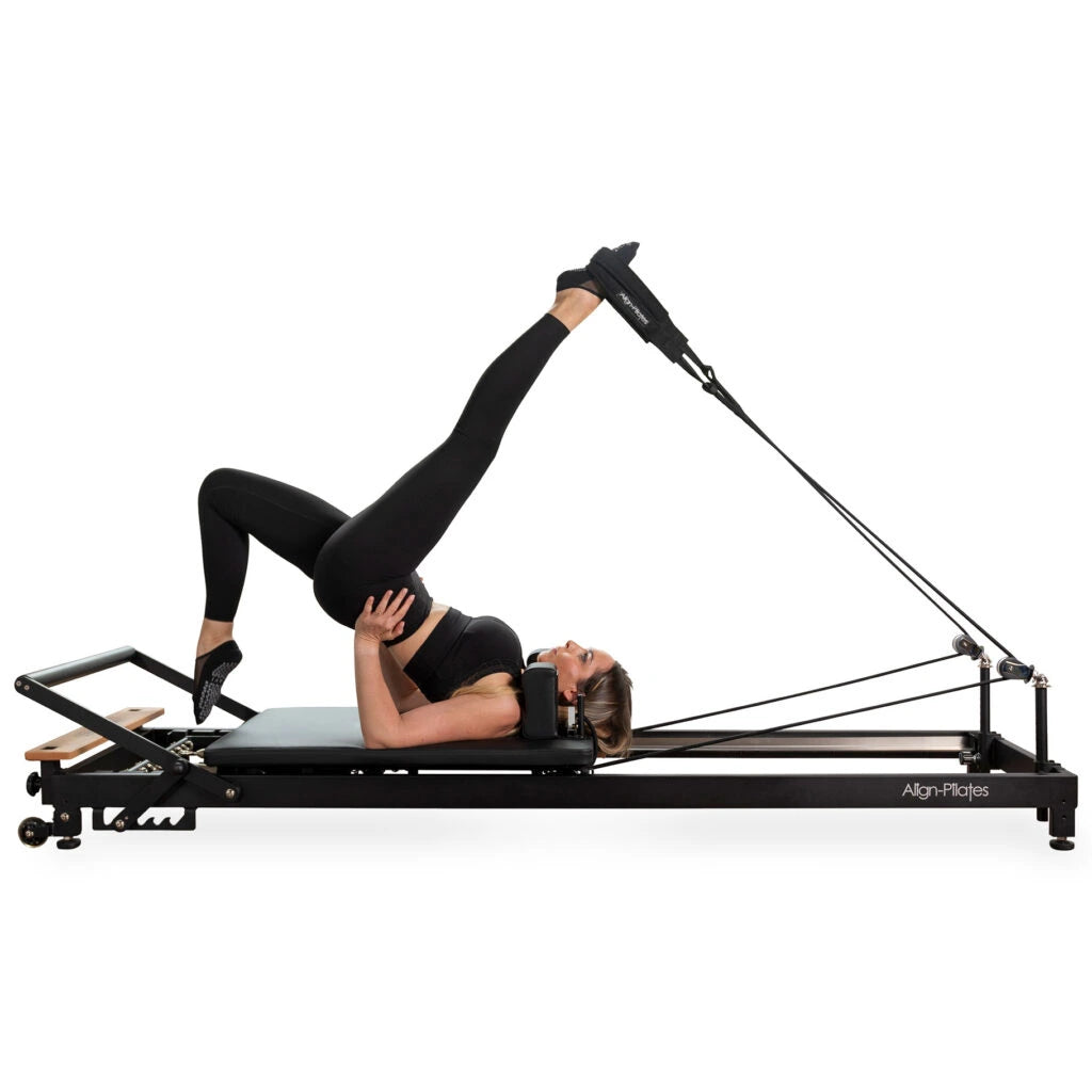 Frau bei einer Beinübung in den Schlaufen auf dem Align Pilates R8-Pro Reformer in Schwarz
