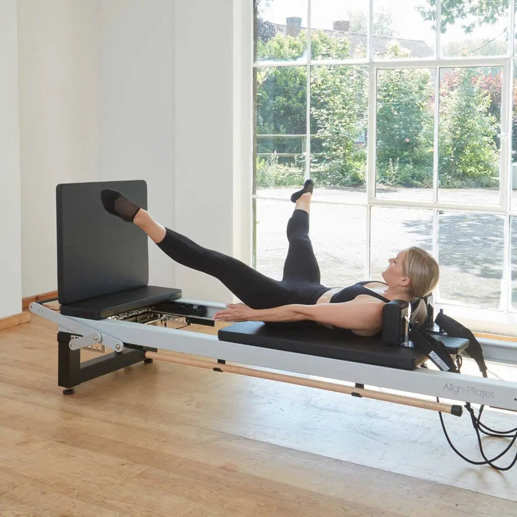 Frau bei einer Sprung-Übung am Align-Pilates Jump Board – auf dem Reformer liegend mit Beinen gegen die schwarze Sprungplattform, Seitenansicht